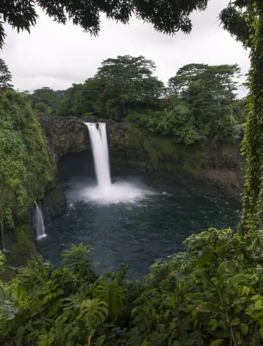 Wailuku River State Park Rainbow Falls cascading into a pool surrounded by dense tropical vegetation.