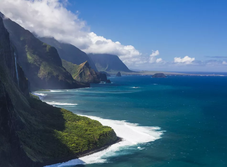 A breathtaking view of Kalaupapa National Historical Park with towering sea cliffs, lush greenery, and the deep blue Pacific Ocean.