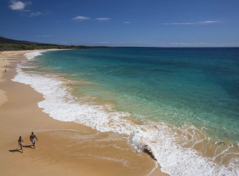 A serene Maui beach with turquoise waters and golden sand under a bright blue sky.
