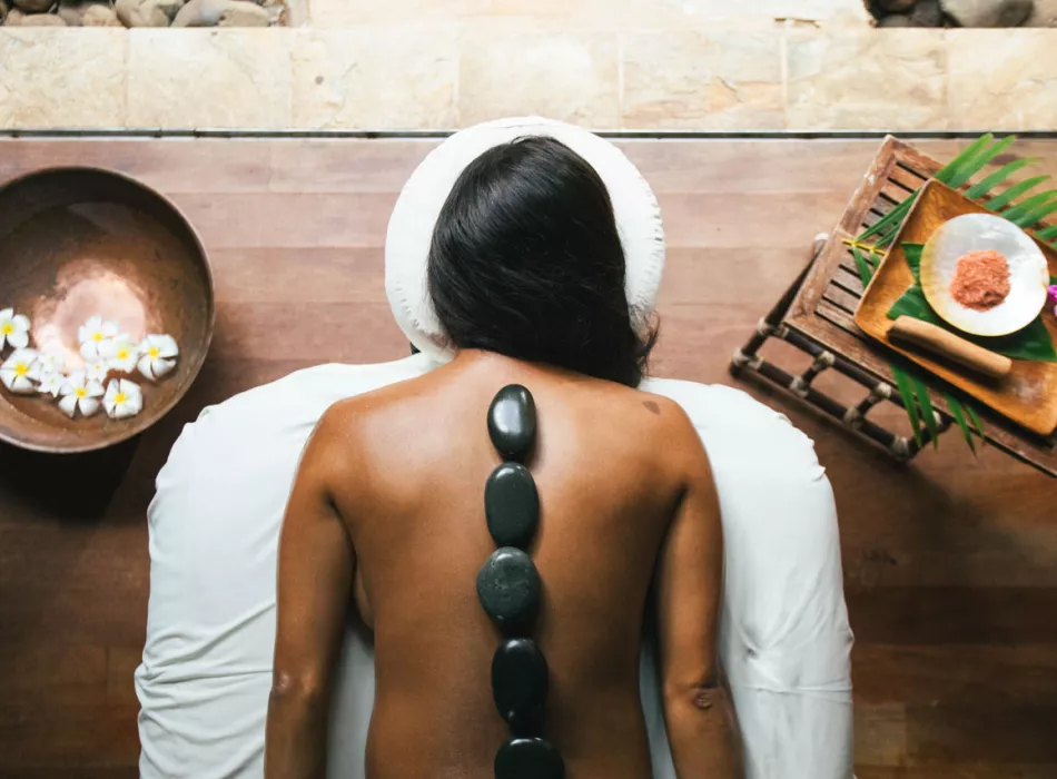 A back massage with hot black stones placed in a line on a woman's spine.